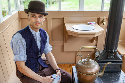 A man dressed as a Victorian horse tram driver sat inside a shelter having a cup of tea